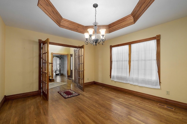 empty room with an inviting chandelier, a tray ceiling, ornamental molding, and hardwood / wood-style flooring