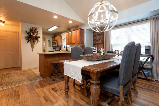 dining space featuring vaulted ceiling, sink, a chandelier, and hardwood / wood-style flooring