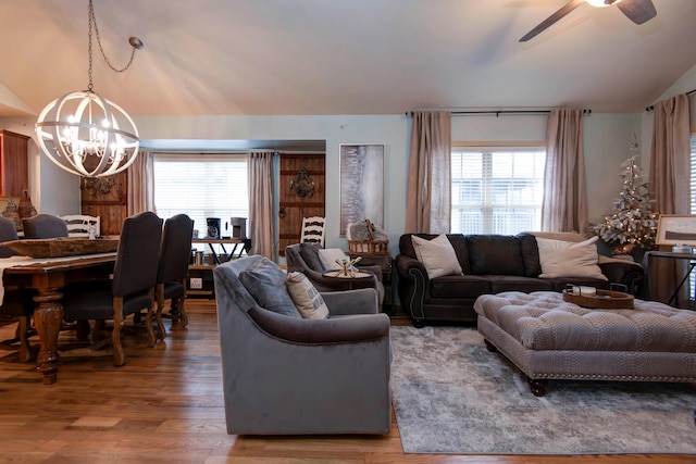 living room featuring vaulted ceiling, ceiling fan with notable chandelier, and wood-type flooring