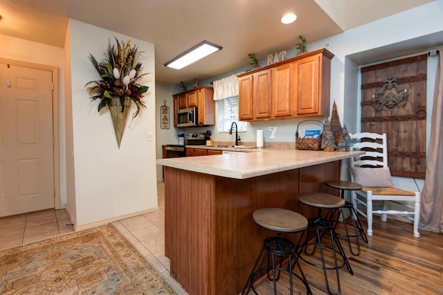 kitchen featuring light tile patterned floors, a kitchen bar, kitchen peninsula, appliances with stainless steel finishes, and sink