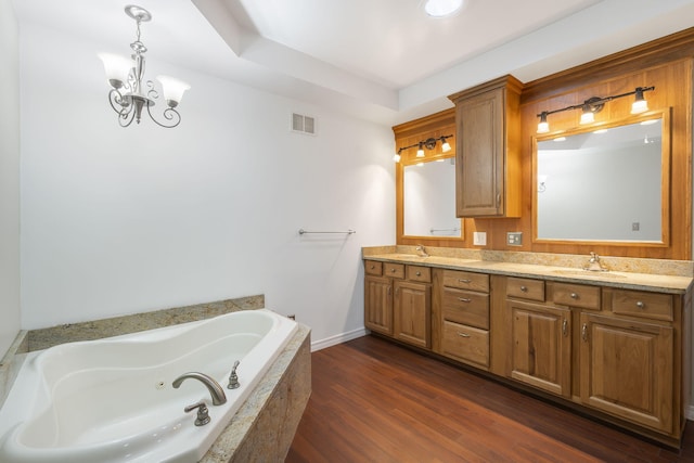 bathroom featuring tiled bath, wood-type flooring, vanity, and a notable chandelier