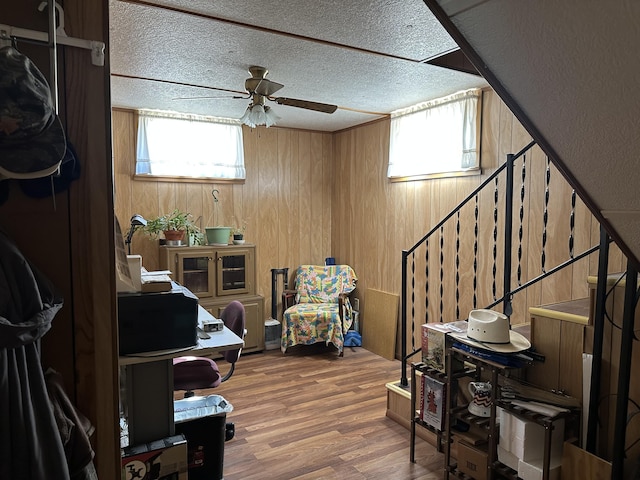 interior space with ceiling fan, wood walls, a textured ceiling, and hardwood / wood-style floors