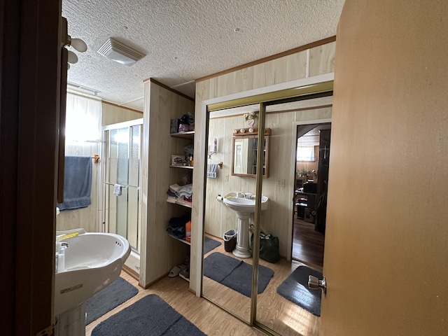 bathroom with a textured ceiling, an enclosed shower, sink, wood walls, and hardwood / wood-style flooring