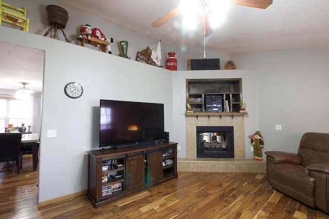 living room featuring hardwood / wood-style flooring, ceiling fan, and a tiled fireplace