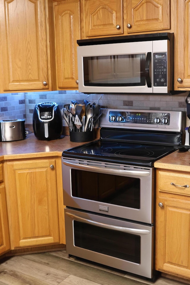 kitchen with double oven range, backsplash, and light hardwood / wood-style floors