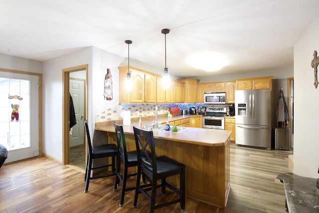 kitchen with backsplash, appliances with stainless steel finishes, kitchen peninsula, and a breakfast bar area