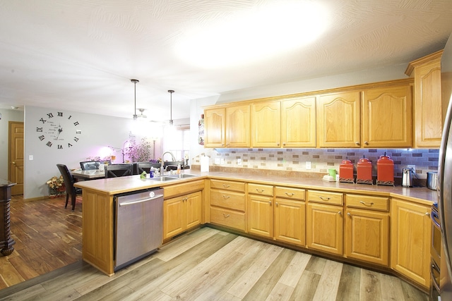 kitchen featuring dishwasher, sink, hanging light fixtures, kitchen peninsula, and light hardwood / wood-style flooring