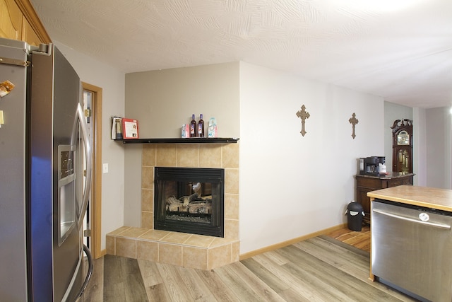 interior space with stainless steel appliances, a tiled fireplace, and light wood-type flooring