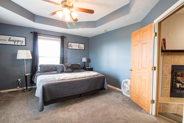 carpeted bedroom with a raised ceiling, ceiling fan, and a tiled fireplace