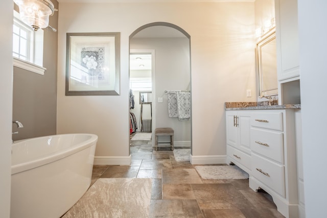 full bathroom with vanity, a freestanding bath, stone finish flooring, and baseboards