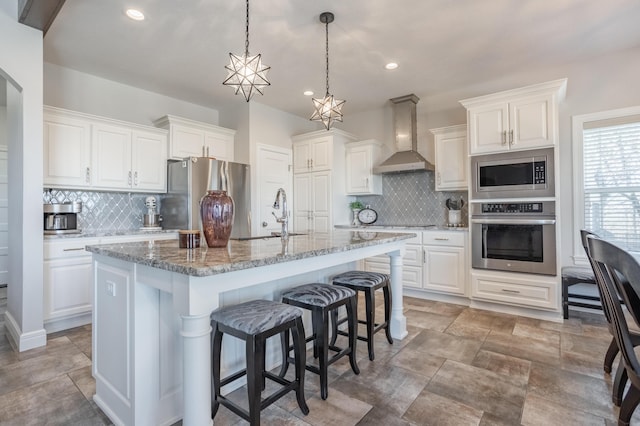 kitchen with a sink, appliances with stainless steel finishes, white cabinetry, a kitchen breakfast bar, and wall chimney exhaust hood