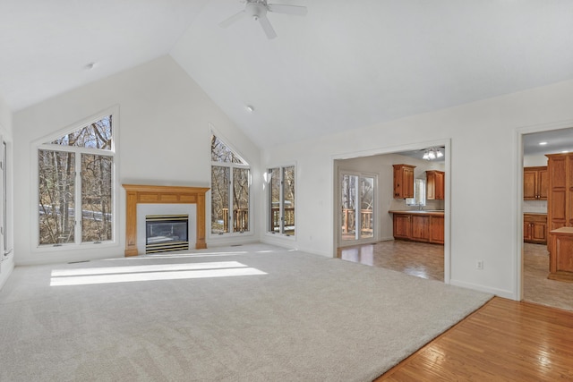 unfurnished living room with light carpet, a wealth of natural light, high vaulted ceiling, and ceiling fan