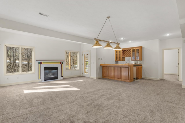 unfurnished living room with light colored carpet, bar, and a tiled fireplace