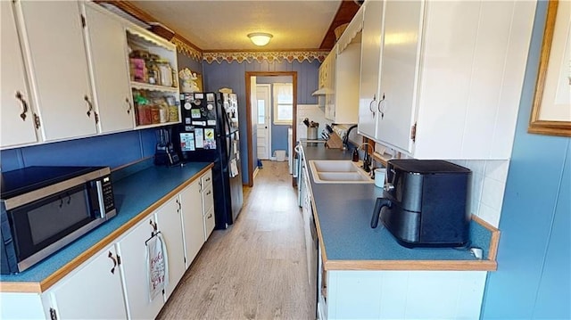 kitchen featuring white cabinets, sink, black fridge, and light hardwood / wood-style floors