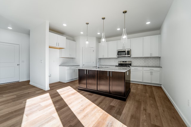 kitchen featuring an island with sink, light stone counters, stainless steel appliances, and white cabinetry