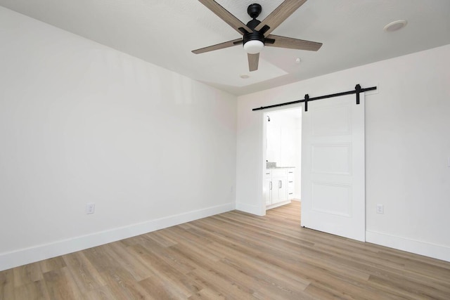 unfurnished bedroom featuring light wood-style floors, a barn door, baseboards, and ceiling fan