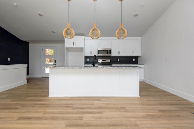 kitchen with light wood finished floors, appliances with stainless steel finishes, white cabinets, and backsplash