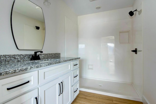 bathroom with a shower, wood finished floors, vanity, and baseboards