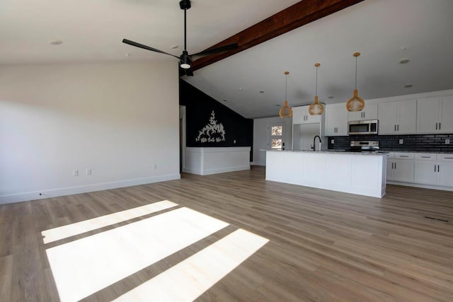 kitchen featuring vaulted ceiling with beams, stainless steel appliances, white cabinetry, open floor plan, and light wood-type flooring