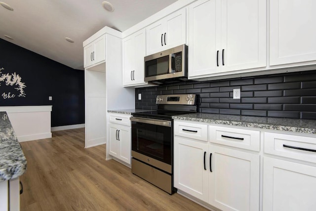 kitchen featuring light stone counters, tasteful backsplash, appliances with stainless steel finishes, white cabinets, and light wood-type flooring