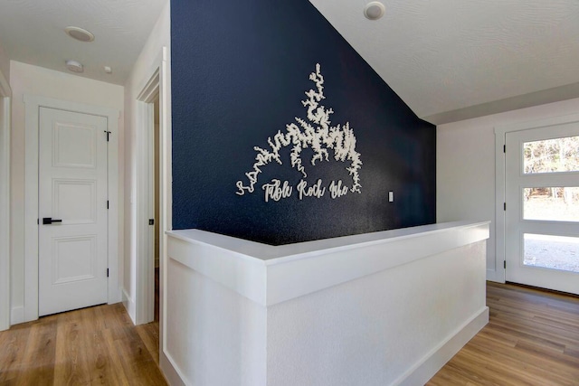 hallway featuring baseboards, vaulted ceiling, and wood finished floors