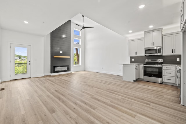 kitchen featuring white cabinetry, appliances with stainless steel finishes, tasteful backsplash, light wood-type flooring, and a fireplace