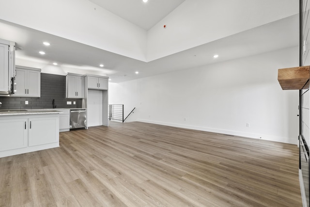 kitchen featuring light hardwood / wood-style floors, a high ceiling, dishwasher, and tasteful backsplash