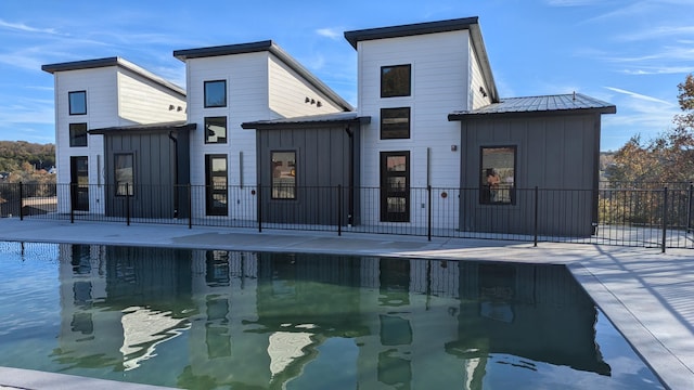 back of property with metal roof, fence, a fenced in pool, board and batten siding, and a patio area