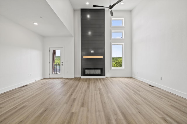 unfurnished living room with ceiling fan, a large fireplace, light wood-type flooring, and a healthy amount of sunlight