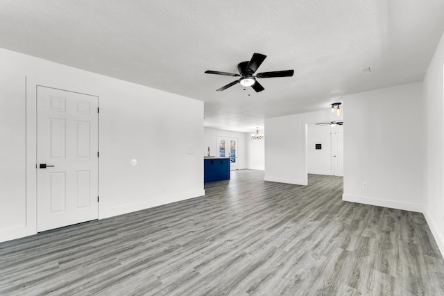 unfurnished living room featuring ceiling fan with notable chandelier, a textured ceiling, and light wood-type flooring