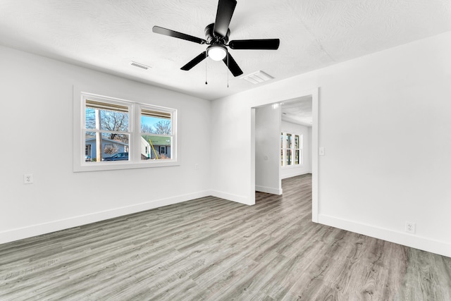 empty room with ceiling fan, light wood-type flooring, and a textured ceiling