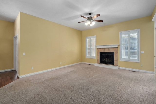 unfurnished living room featuring ceiling fan, plenty of natural light, a tile fireplace, and carpet floors