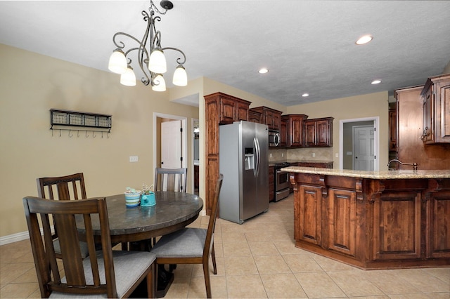 kitchen featuring light stone countertops, decorative light fixtures, stainless steel appliances, backsplash, and light tile patterned floors