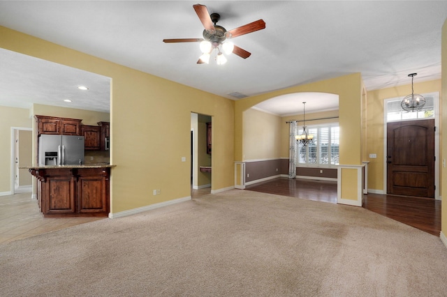 unfurnished living room featuring light colored carpet and ceiling fan with notable chandelier