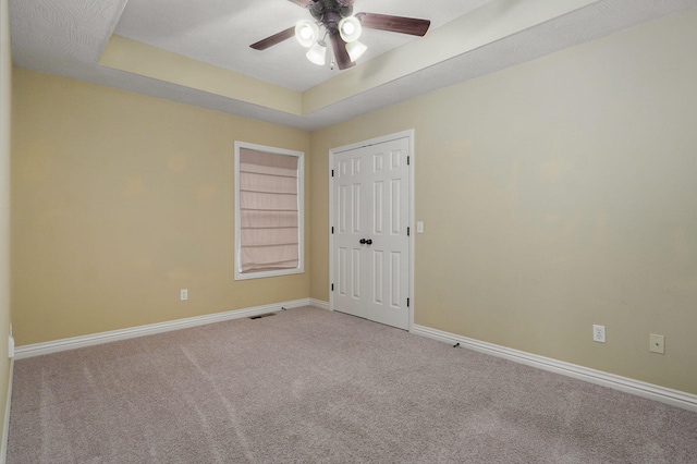 empty room with ceiling fan, carpet, a tray ceiling, and built in shelves