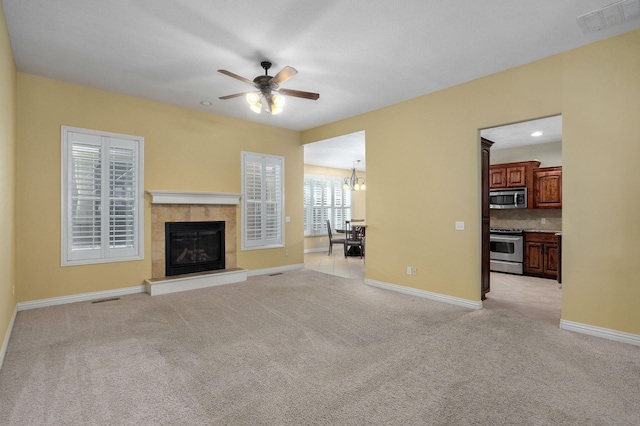 unfurnished living room featuring ceiling fan with notable chandelier, a tile fireplace, and light carpet