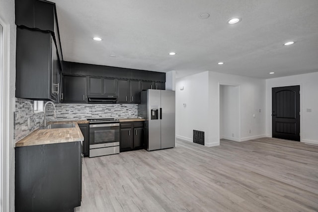 kitchen with ventilation hood, appliances with stainless steel finishes, tasteful backsplash, light wood-type flooring, and sink