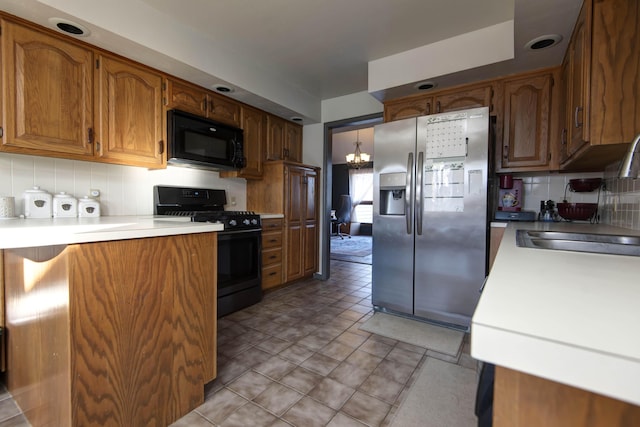 kitchen with sink, backsplash, black appliances, and an inviting chandelier