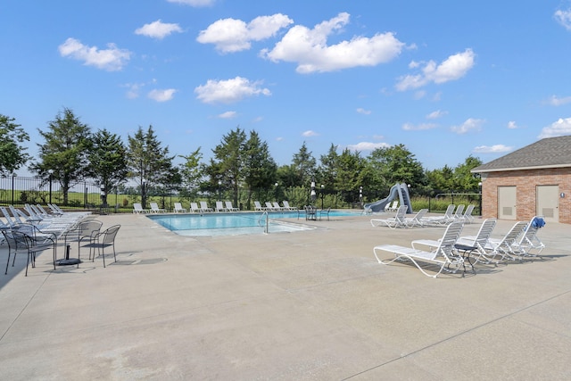 community pool featuring a water slide, fence, and a patio