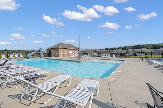 community pool with a patio area, fence, and a water slide