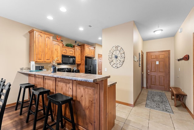 kitchen featuring black appliances, light tile patterned floors, kitchen peninsula, and a breakfast bar area