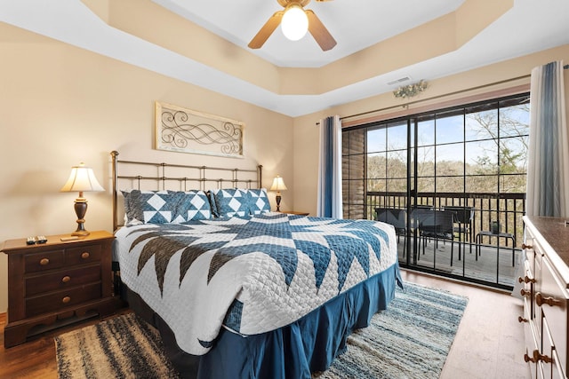 bedroom with hardwood / wood-style flooring, a raised ceiling, and ceiling fan