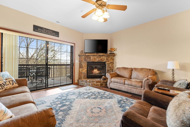 living room with hardwood / wood-style flooring, ceiling fan, and a stone fireplace