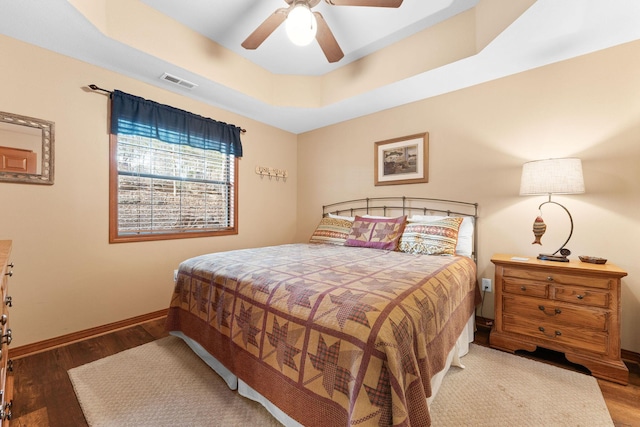 bedroom with ceiling fan, wood-type flooring, and a raised ceiling