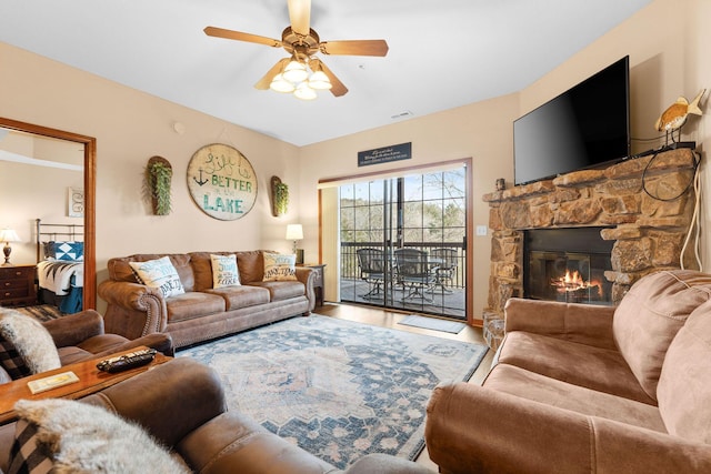 living room with ceiling fan, hardwood / wood-style floors, and a stone fireplace