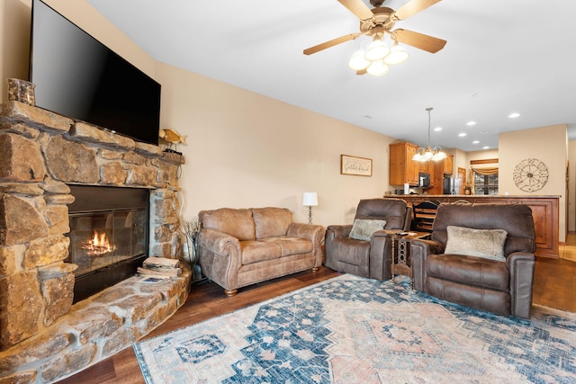 living room with dark hardwood / wood-style flooring, ceiling fan with notable chandelier, and a stone fireplace