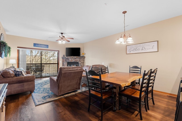 dining room featuring dark hardwood / wood-style flooring, ceiling fan with notable chandelier, and a stone fireplace