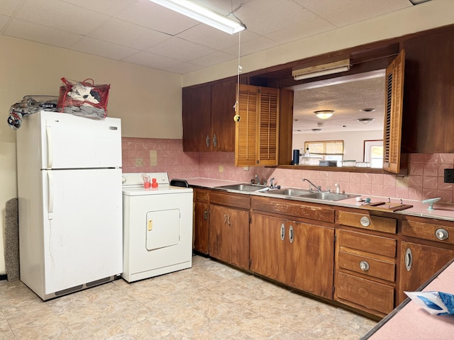 kitchen with white fridge, decorative backsplash, decorative light fixtures, washer / clothes dryer, and sink