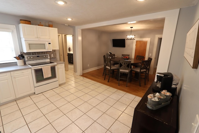 kitchen with white appliances, white cabinets, backsplash, hanging light fixtures, and light tile patterned floors