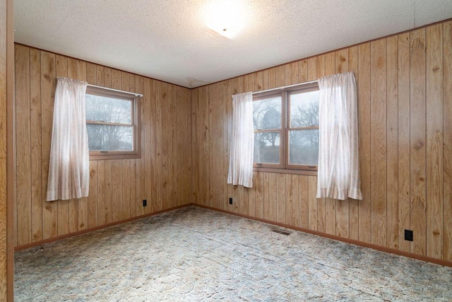 spare room with a healthy amount of sunlight, wooden walls, and a textured ceiling